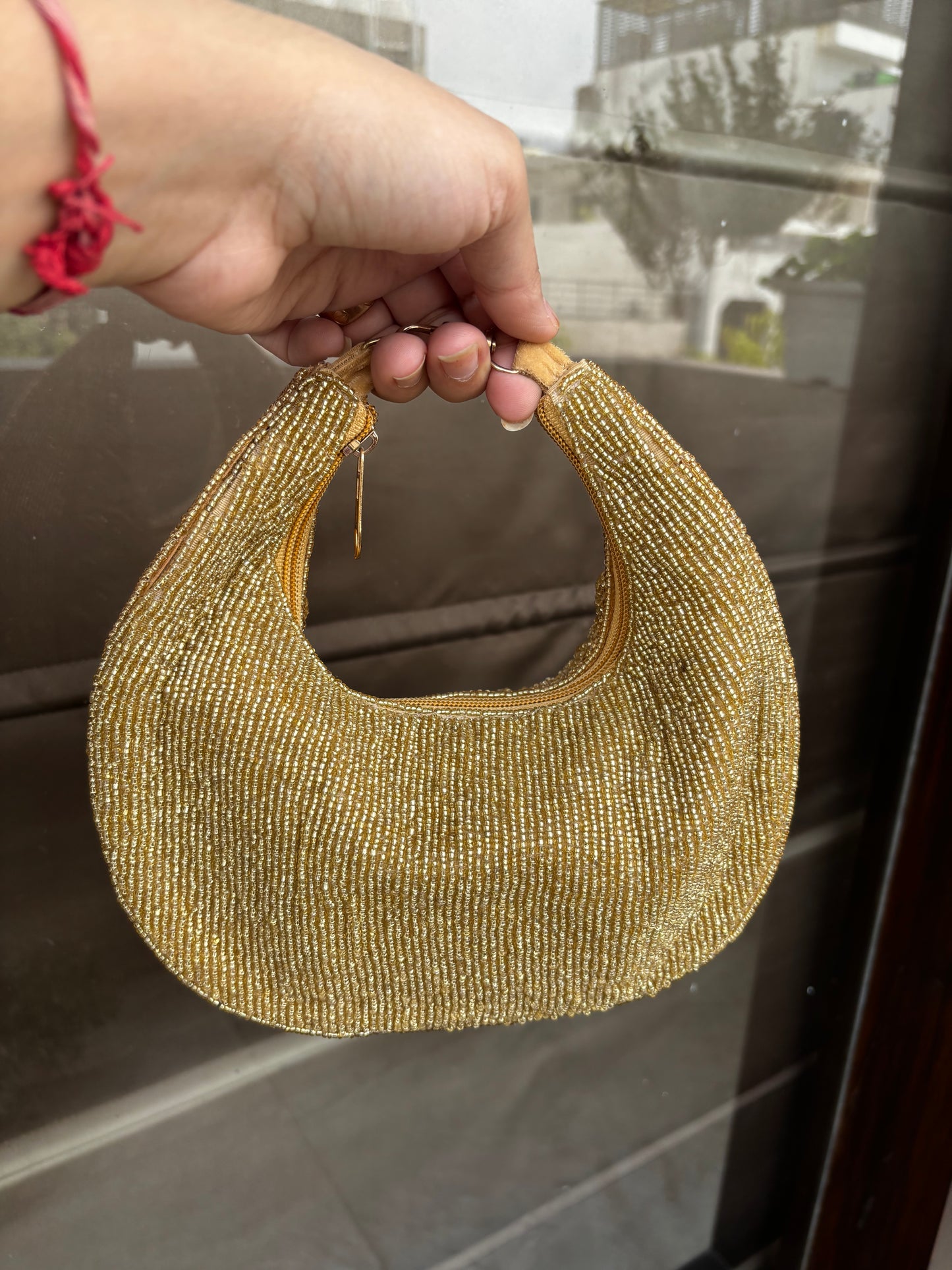 Gold beaded crescent moon ornament held by a hand against a reflective surface.