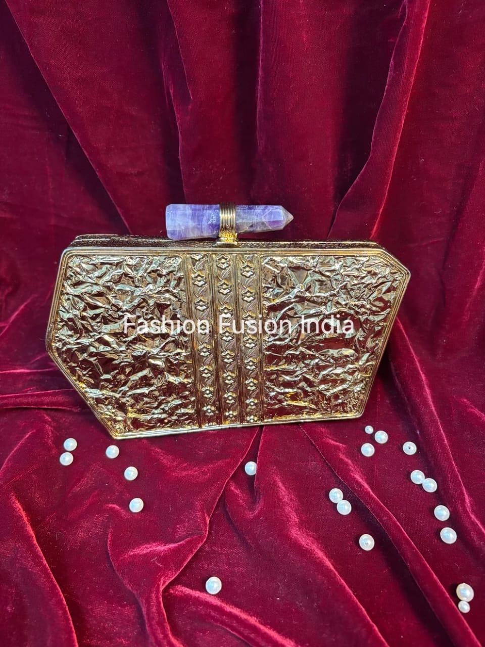 Gold clutch bag on a red velvet background with 'Fashion Fusion India' branding.