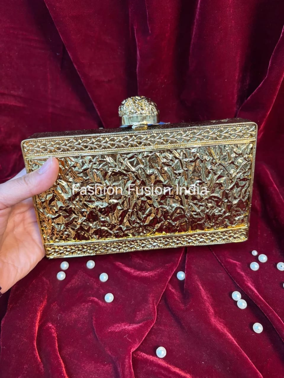 Gold clutch held by a hand on a red velvet background with 'Fashion Fusion India' branding.