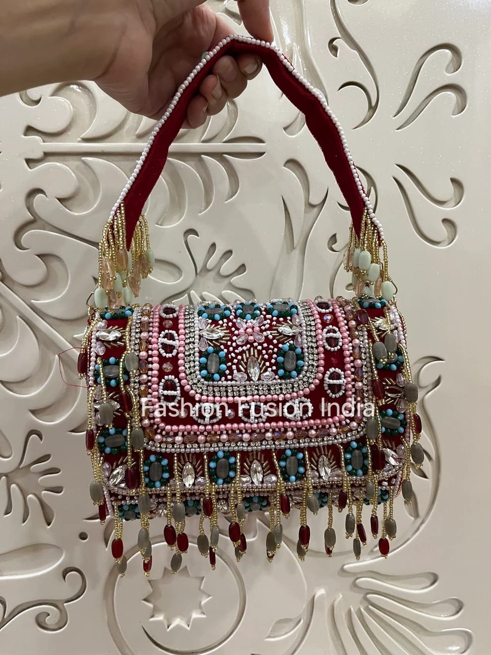 Decorative handbag with intricate designs and embellishments held by a hand against a decorative white background.