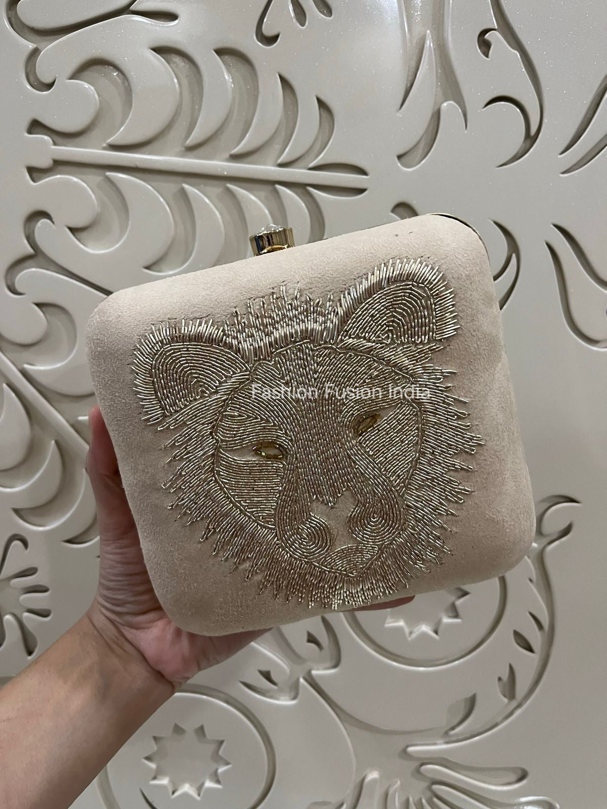 Beige clutch bag with lion embroidery held against a decorative white background