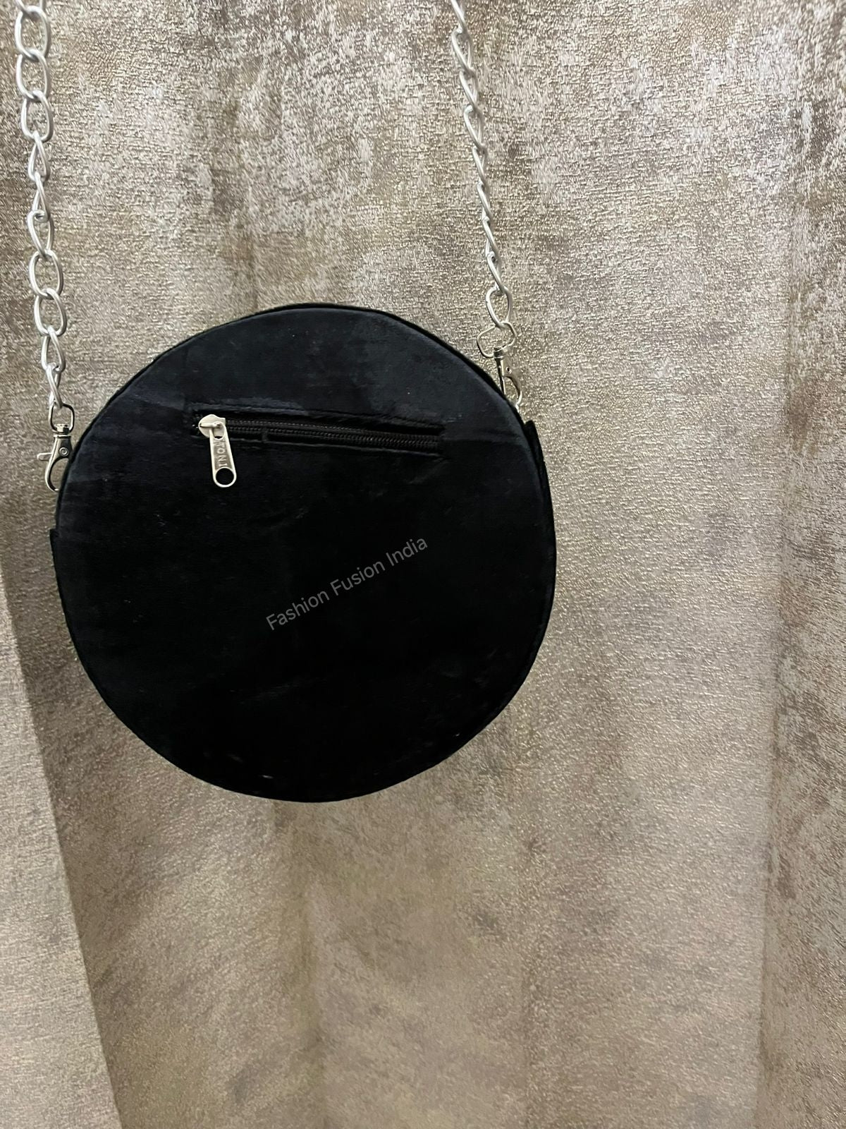 Black round handbag with chain strap on a textured beige background