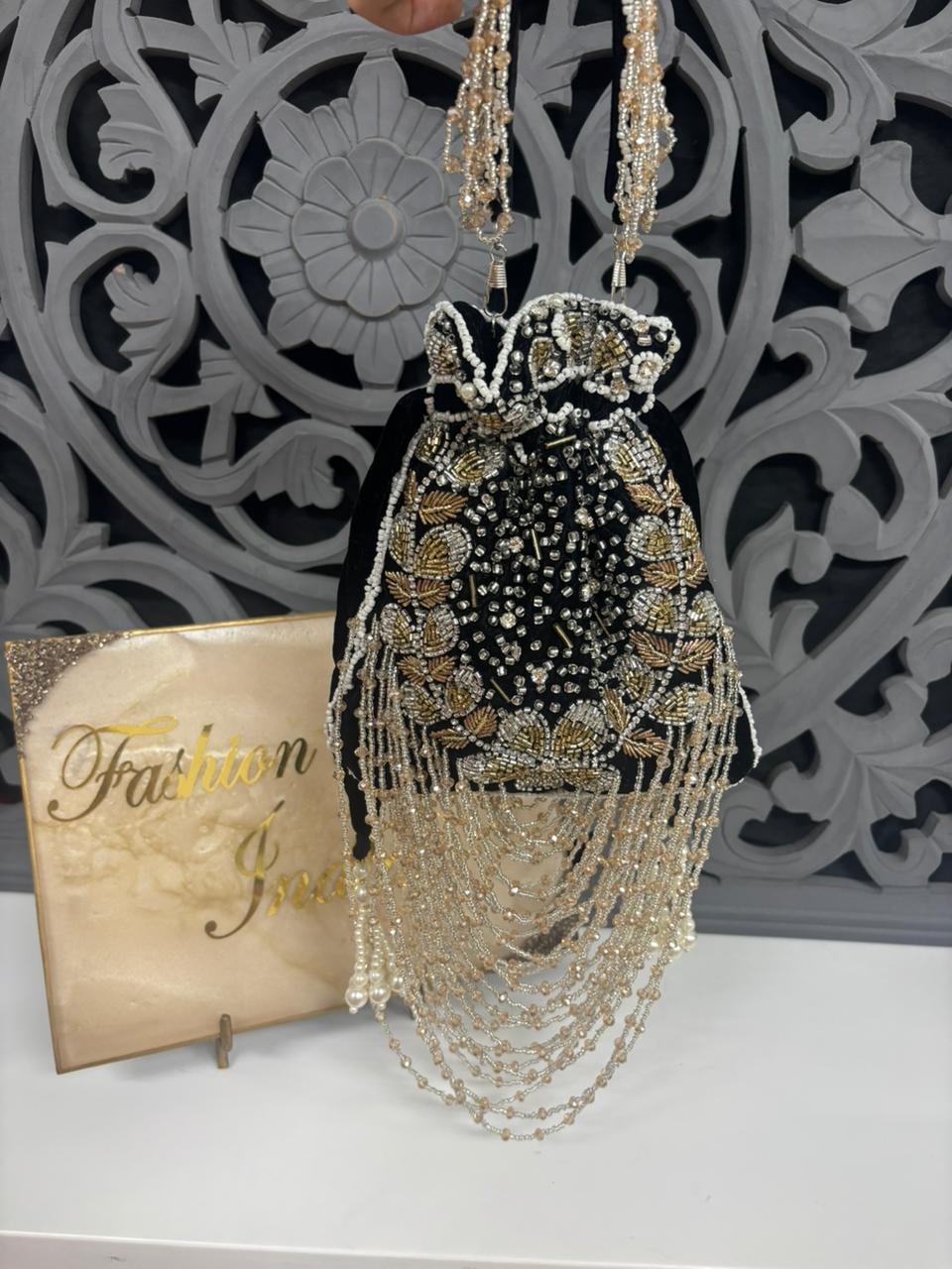 Decorative handbag with gold and black details on a white surface with a decorative wall in the background.