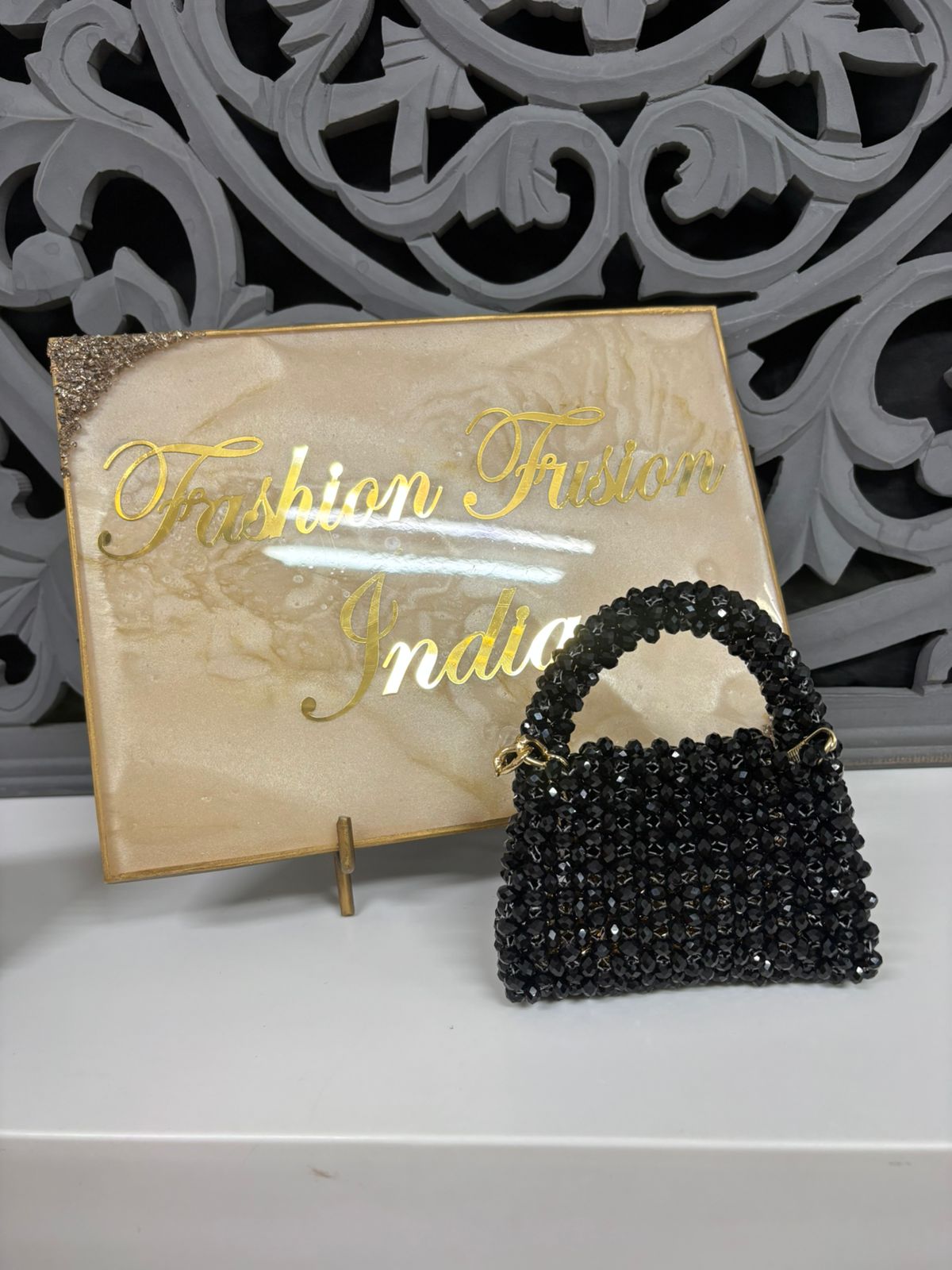 Black beaded handbag in front of a 'Fashion India' sign
