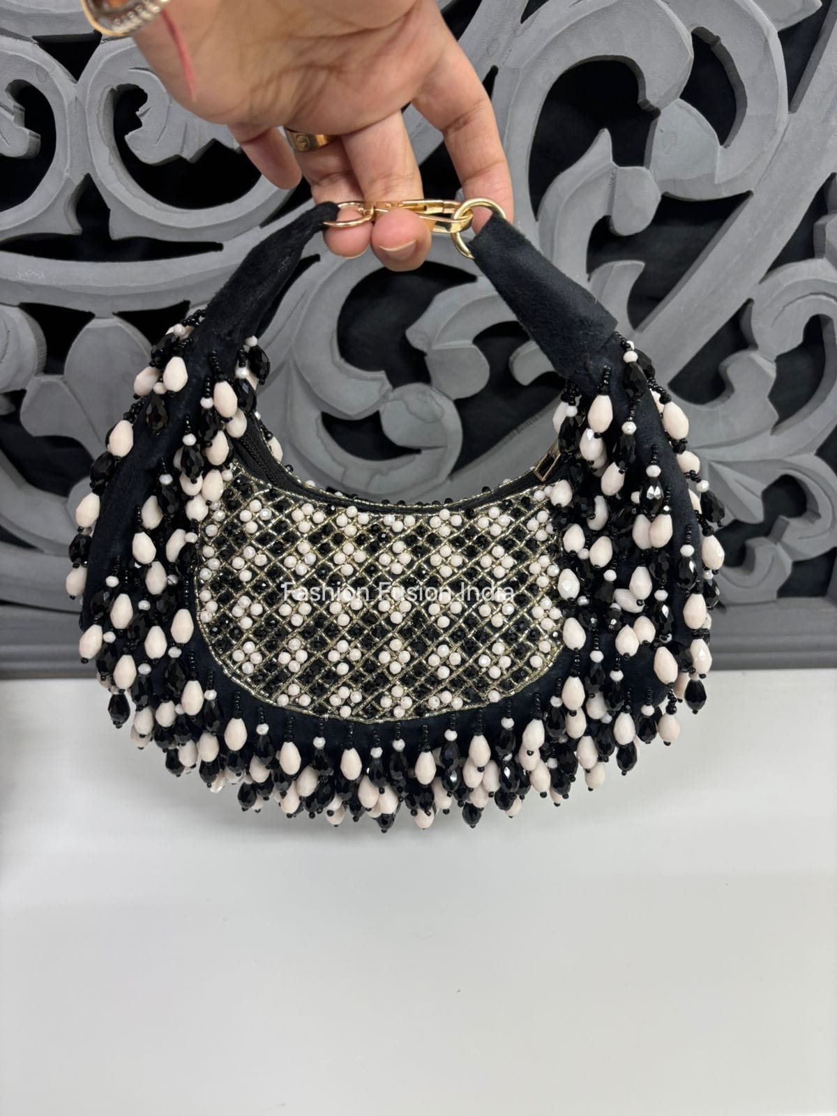 Black handbag with white beads held by a hand against a decorative wall.