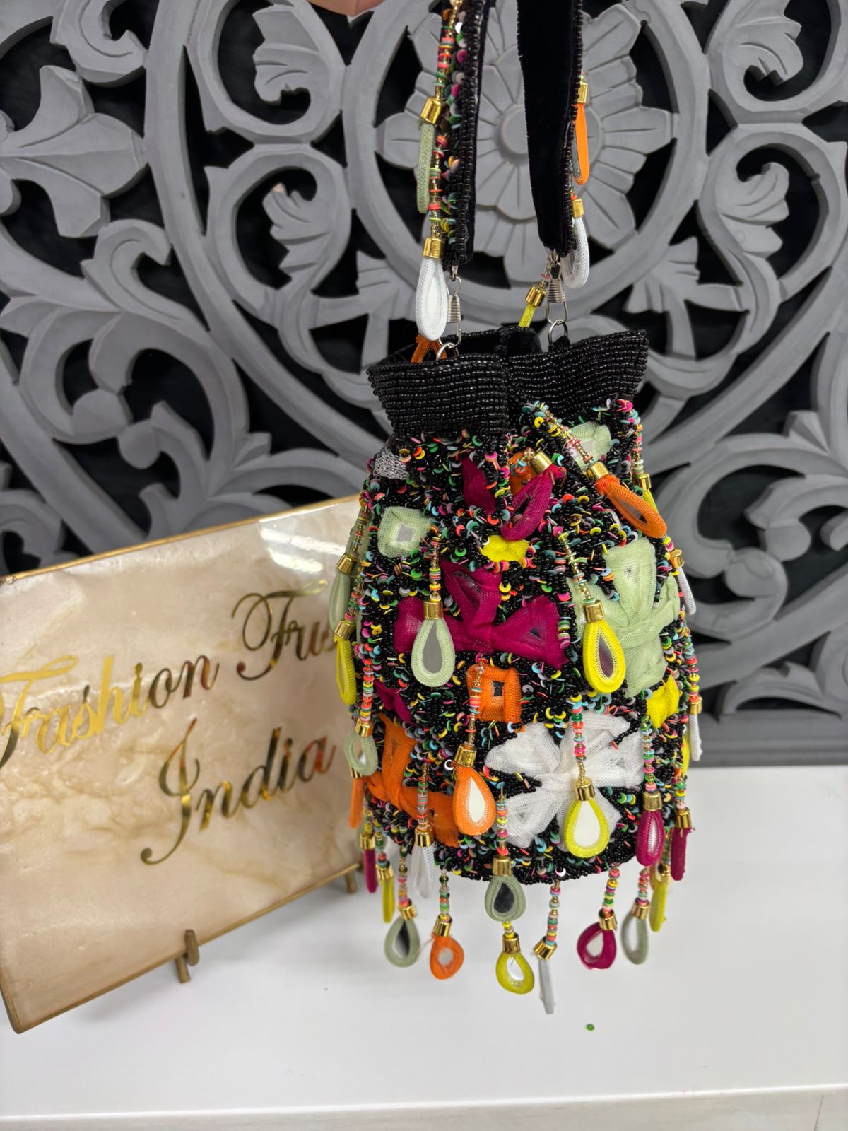 Colorful beaded bag with decorative elements on a white surface with 'Fashion First' sign.