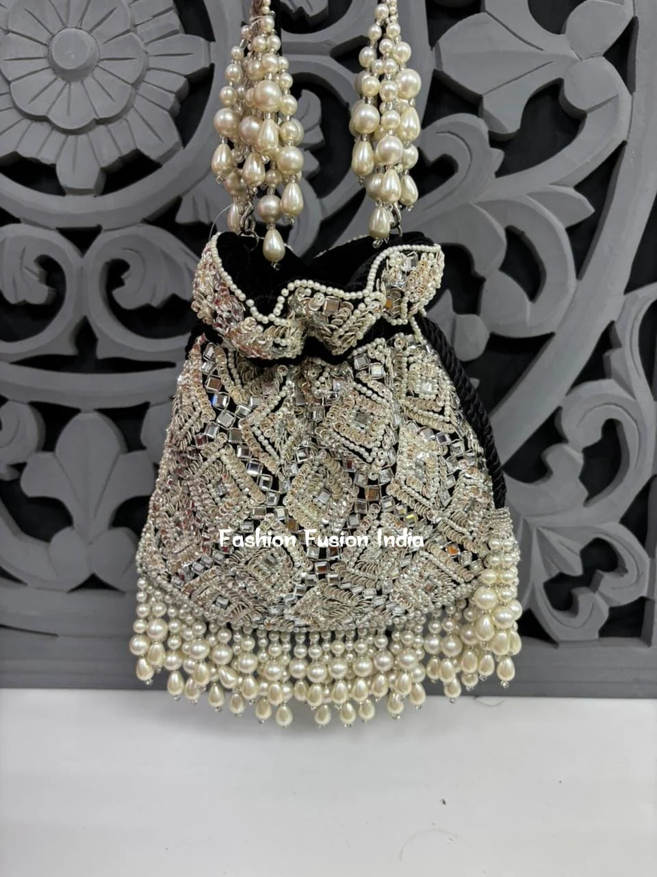 Decorative handbag with pearl details on a white surface with a decorative gray background.