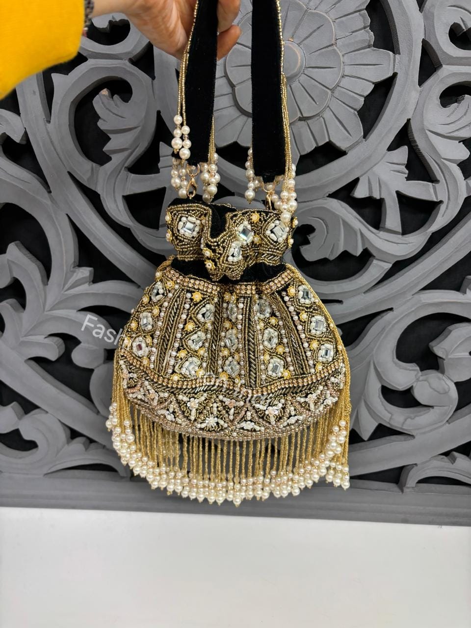 Decorative handbag with gold and pearl details against a decorative wall.
