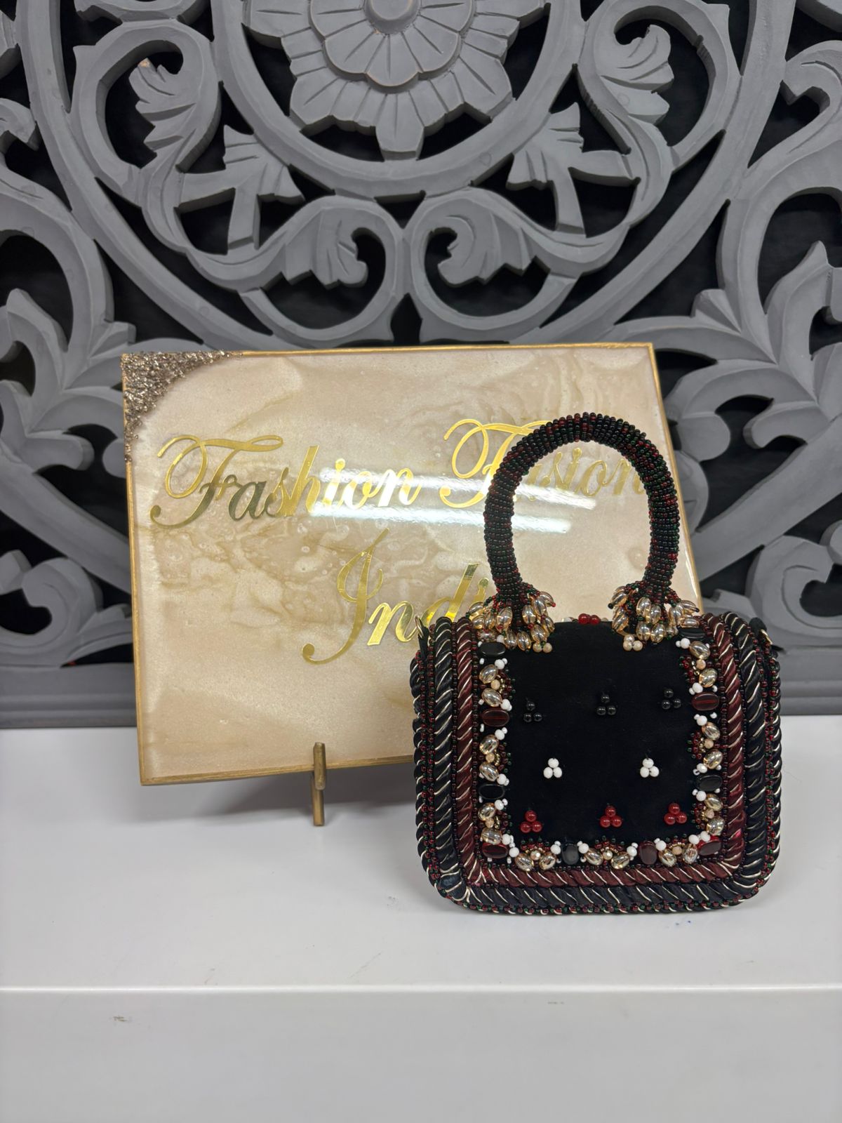 Decorative handbag with intricate design in front of a decorative wall panel.