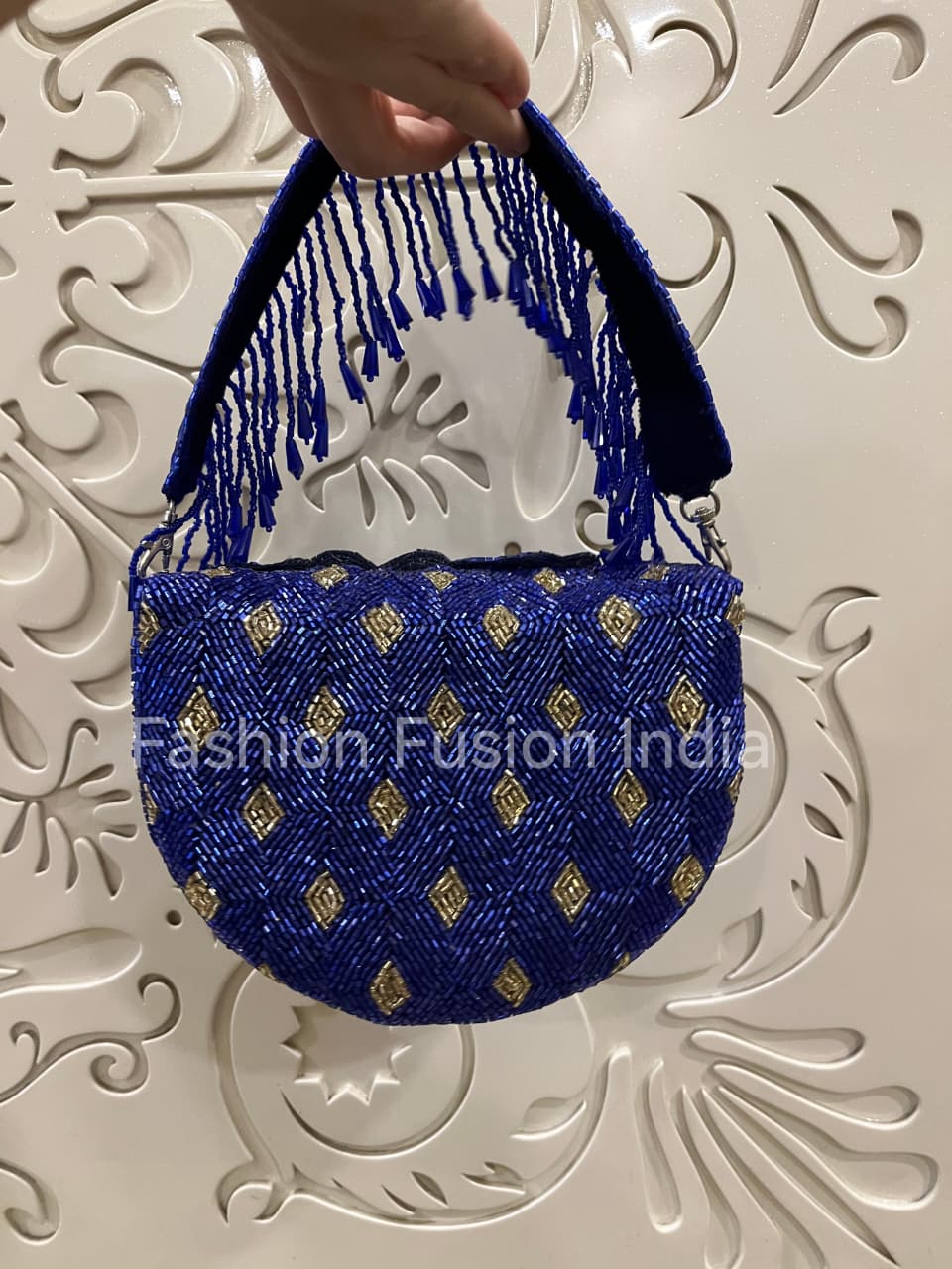 Blue handbag with gold patterns held by a hand against a decorative white background, branded 'Fashion Fusion India'.