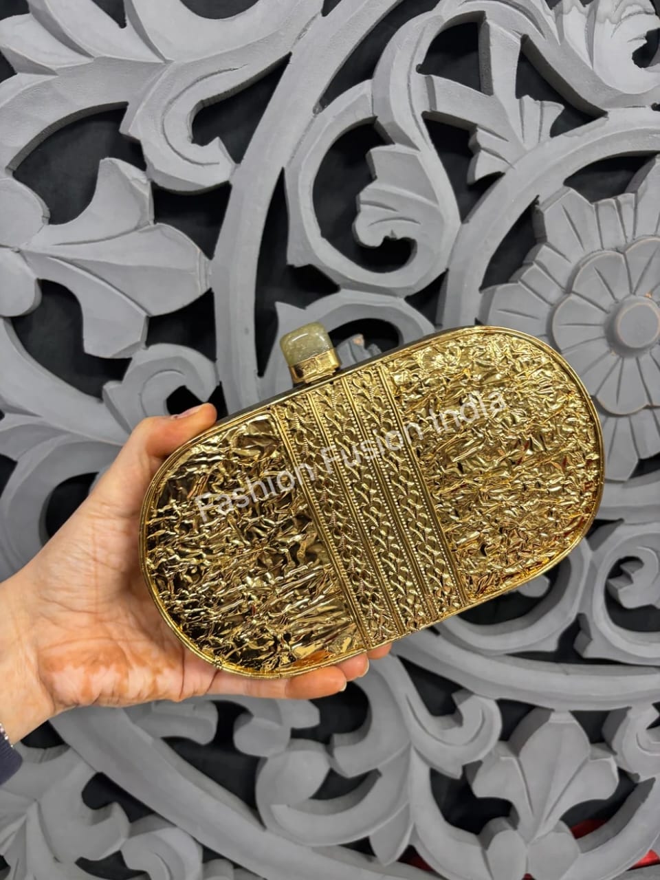 Gold clutch held by a hand against a decorative gray background