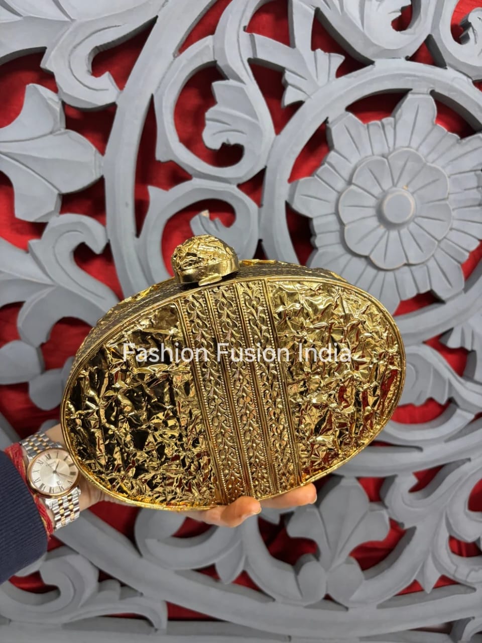 Gold clutch held by a hand with a red and white decorative background