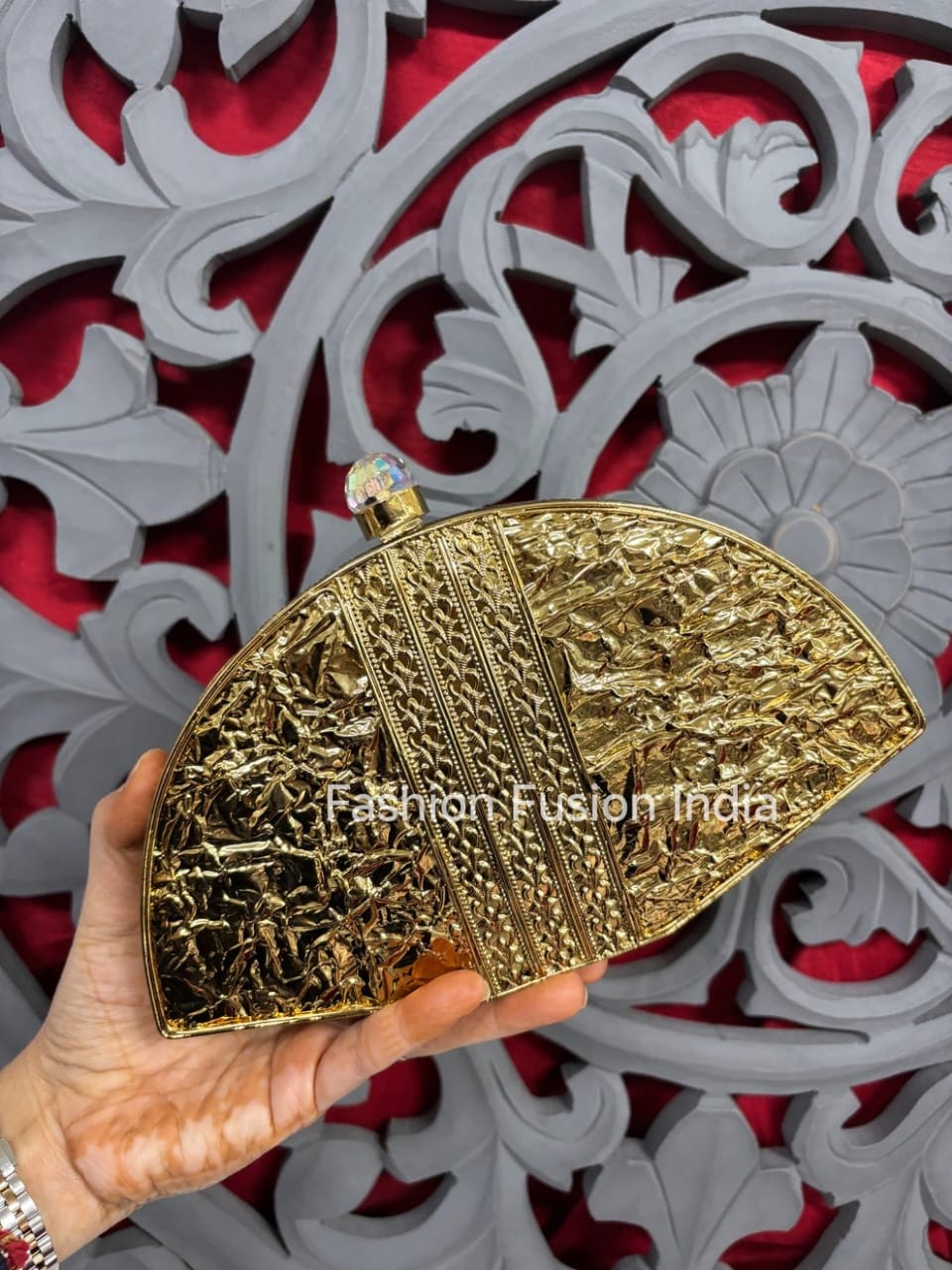 Gold clutch held by a hand with a decorative red and white background