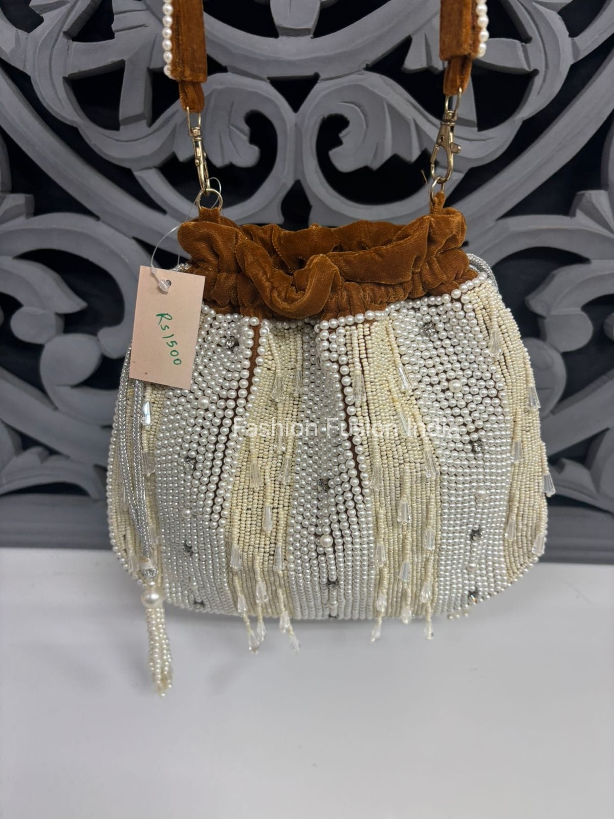 Beaded handbag with fringes and a decorative handle on a gray surface.