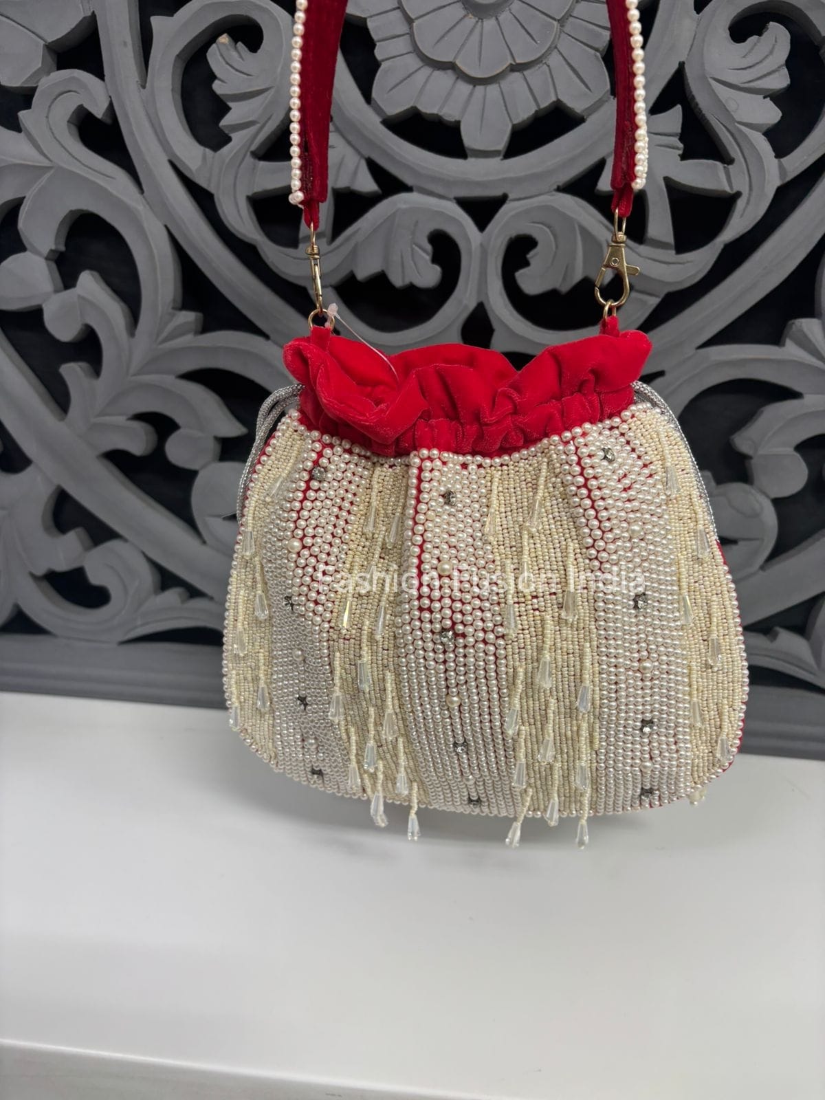 Beaded handbag with red floral top against a decorative wall.