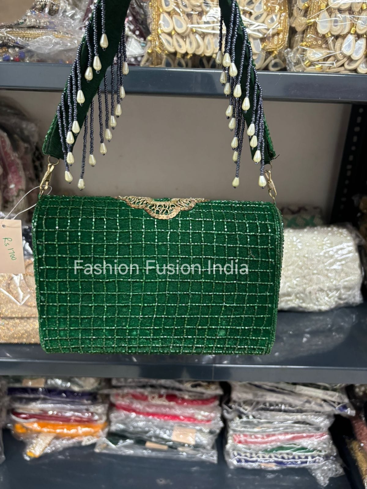 Green handbag with decorative elements on a shelf with 'Fashion Fusion India' branding.