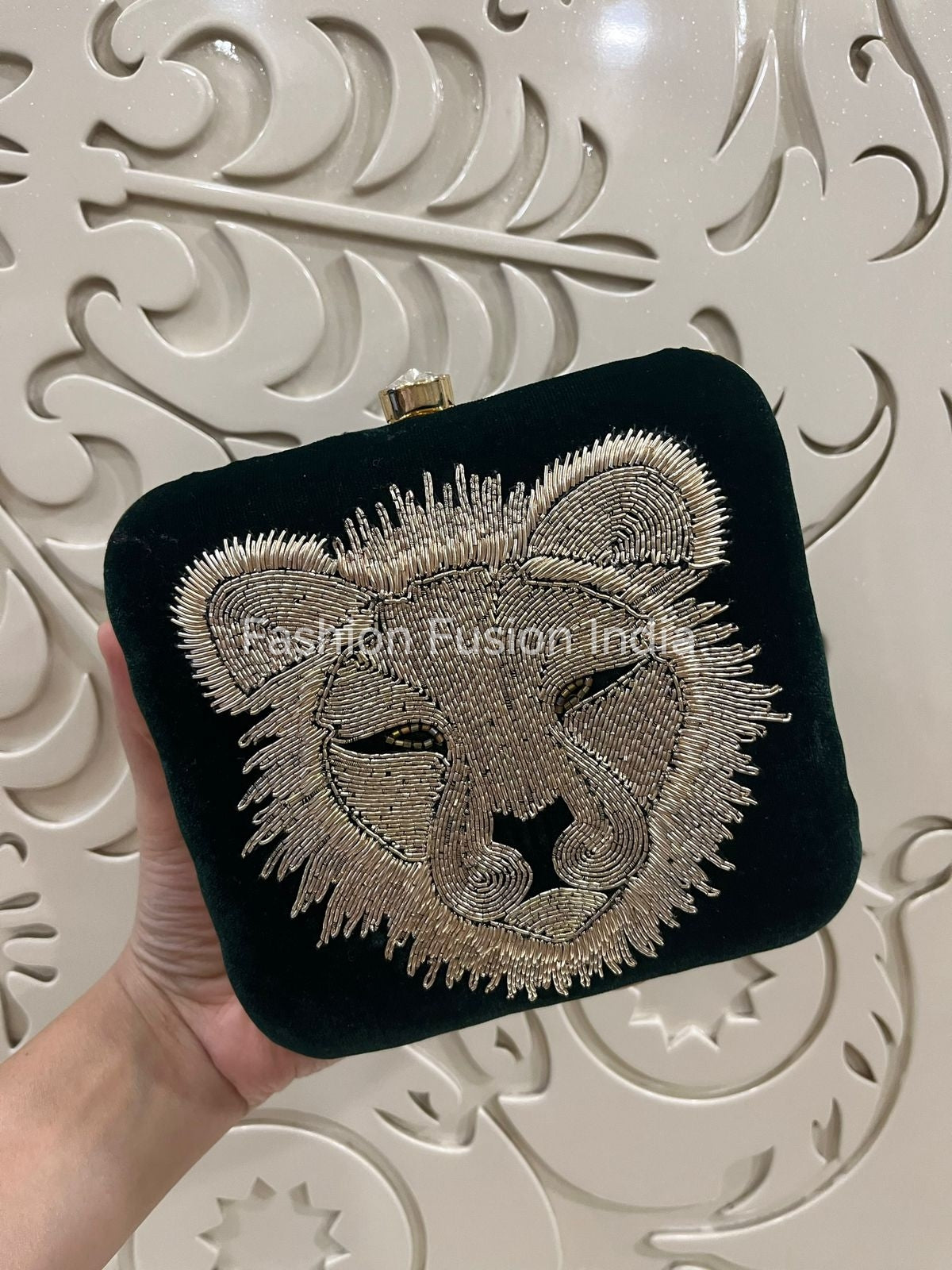 Green clutch with lion embroidery held against a decorative white background