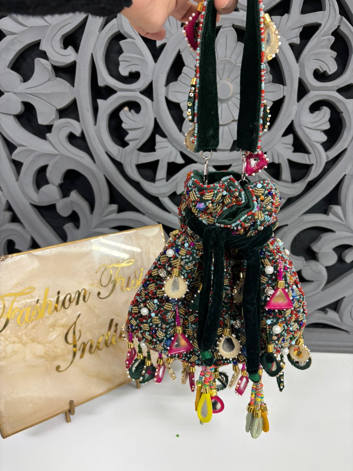 Colorful beaded handbag with decorative elements on a white surface with a decorative gray background.