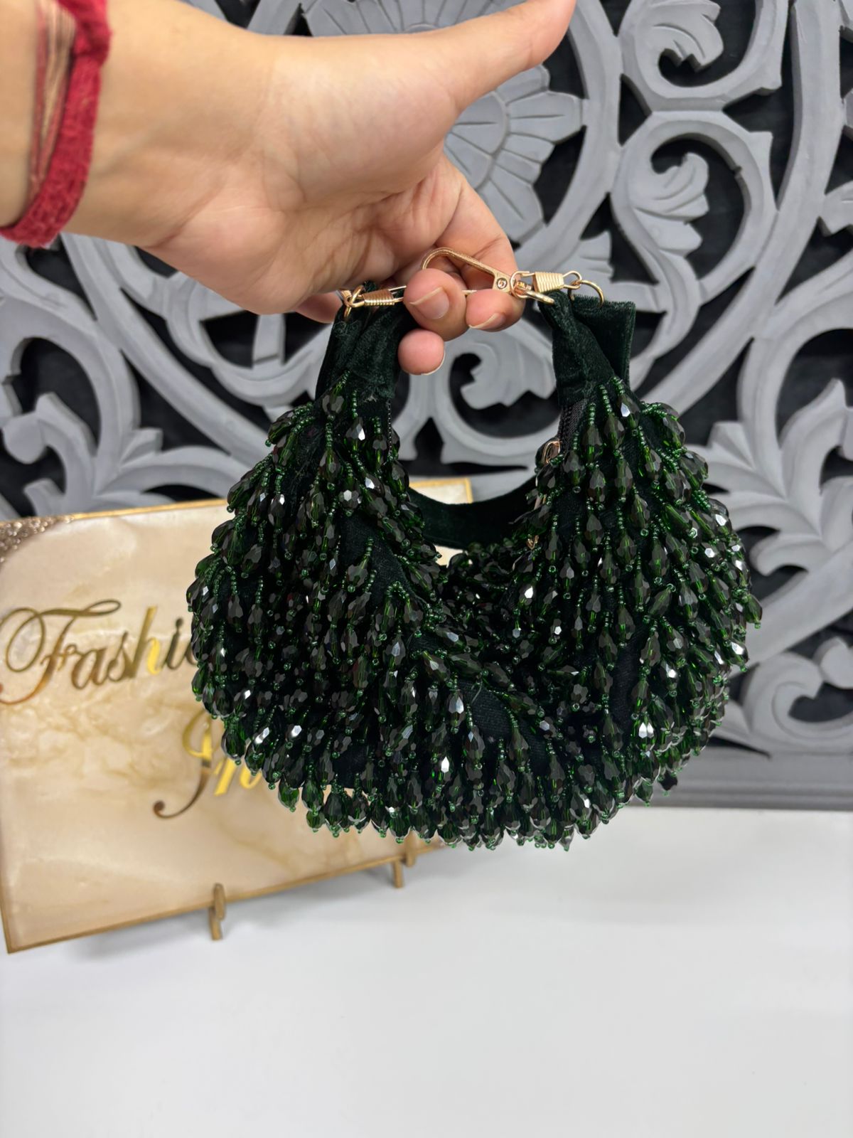 Green beaded handbag held by a hand with a decorative background