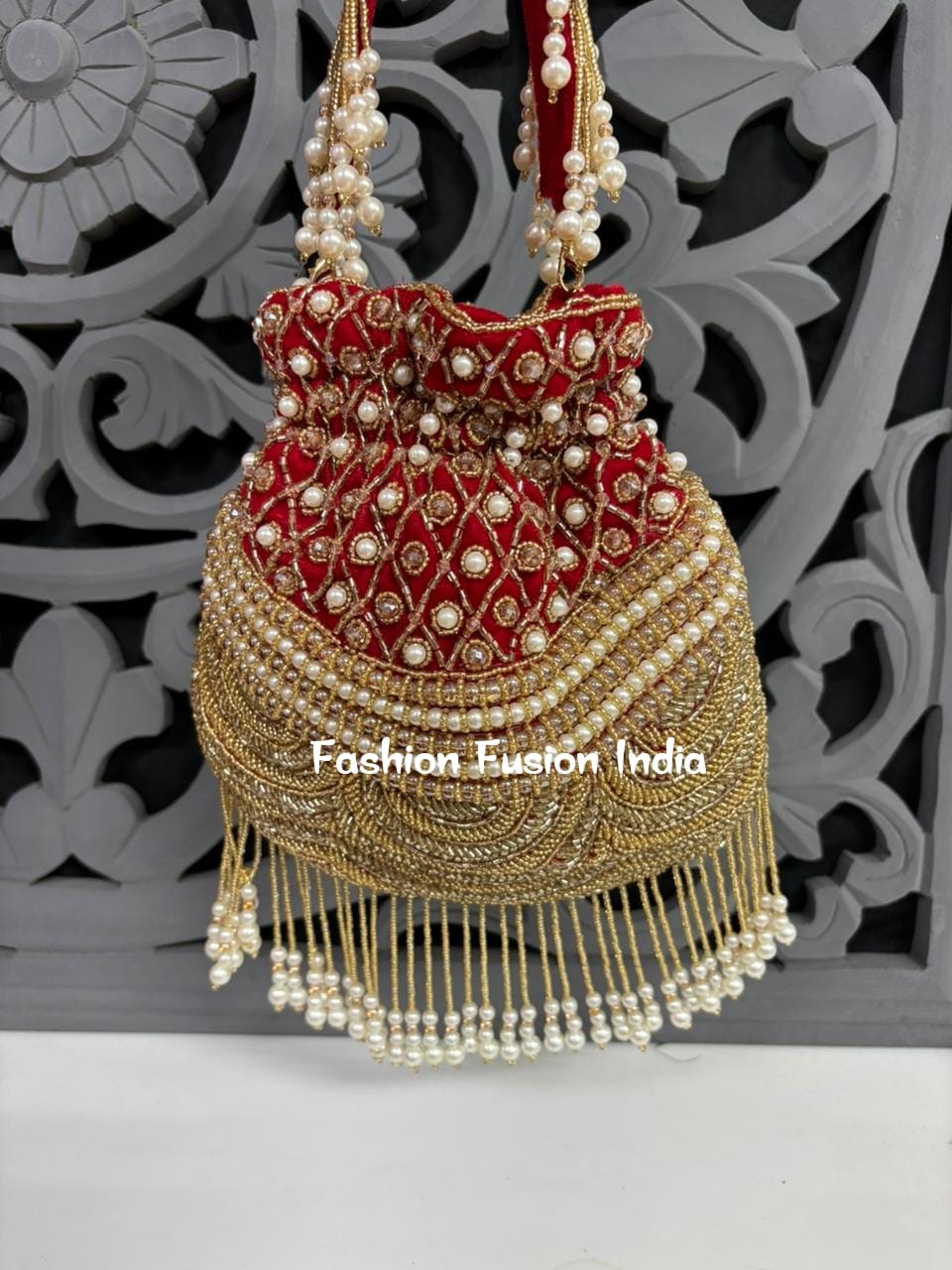 Decorative handbag with pearls and gold details on a white surface with a decorative gray background.