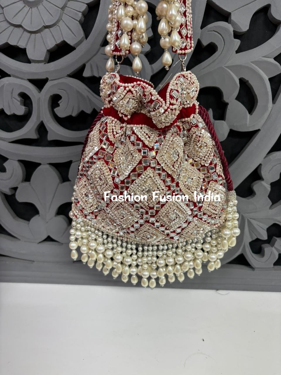 Decorative handbag with pearls and red accents against a decorative gray background
