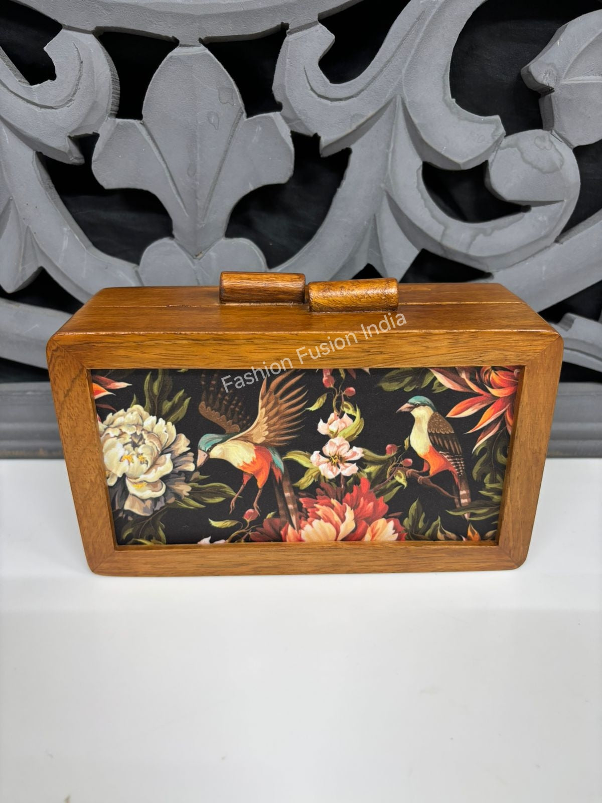 Wooden box with floral and bird design on a white surface with decorative background