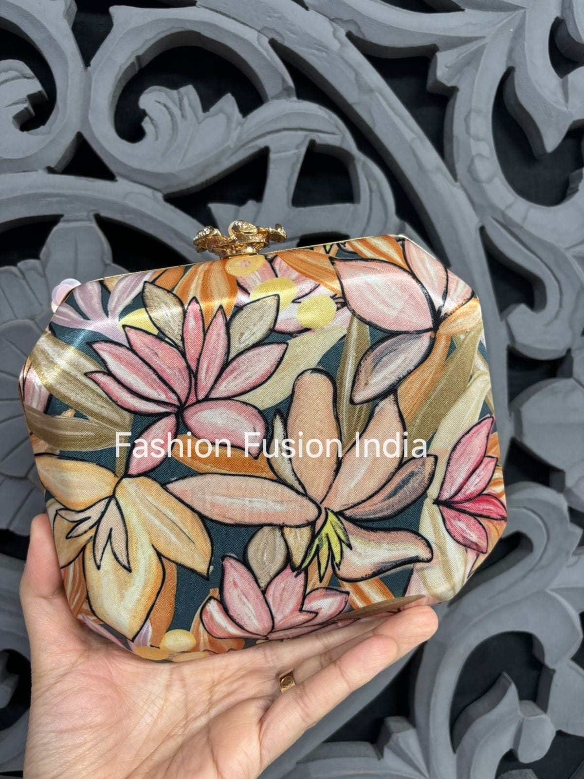 Floral patterned clutch held by a hand against an ornate background with 'Fashion Fusion India' branding.