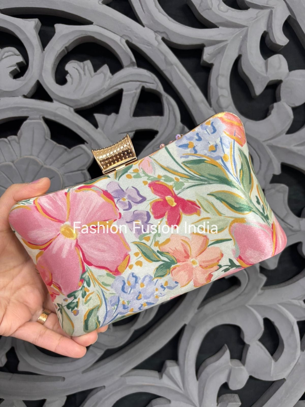 Floral clutch held by a hand against an ornate gray background, with 'Fashion Fusion India' branding.