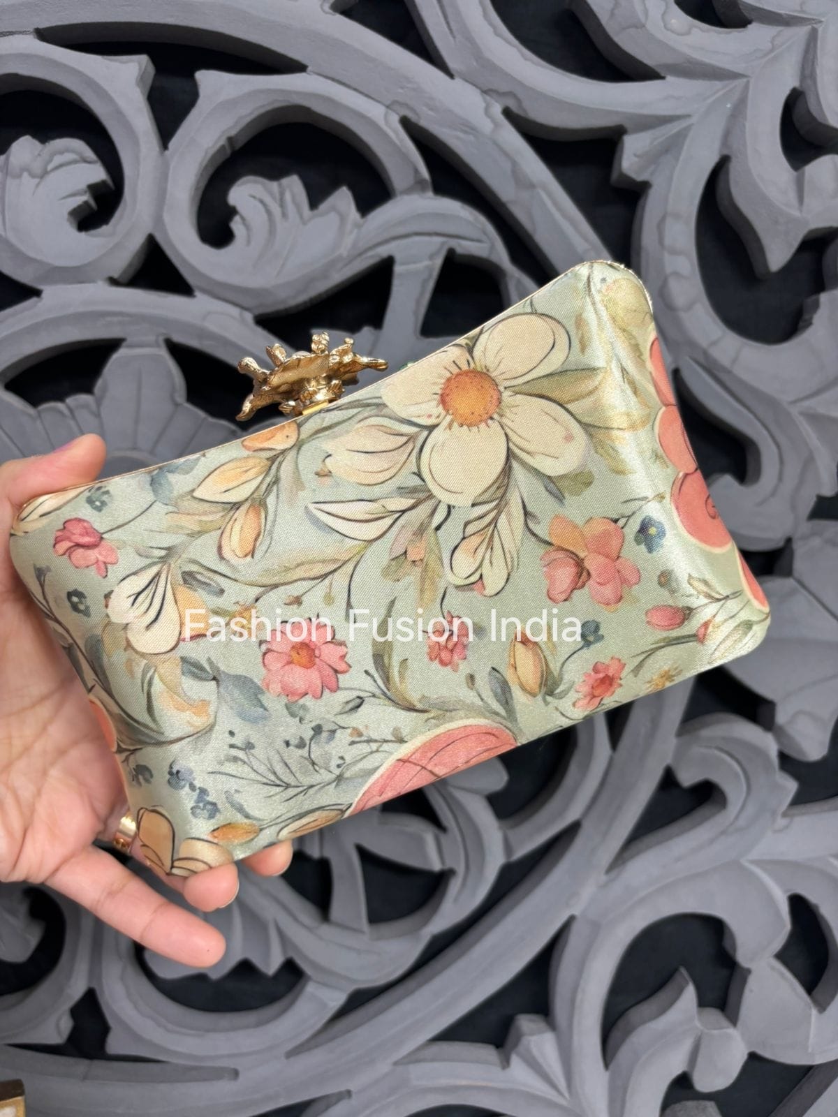 Floral patterned clutch held by a hand against an ornate background