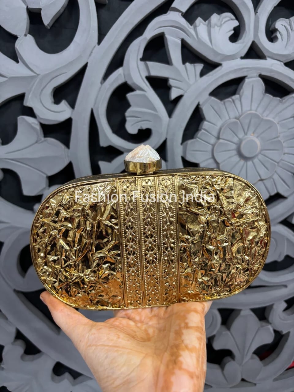 Gold clutch held by a hand with intricate design in the background