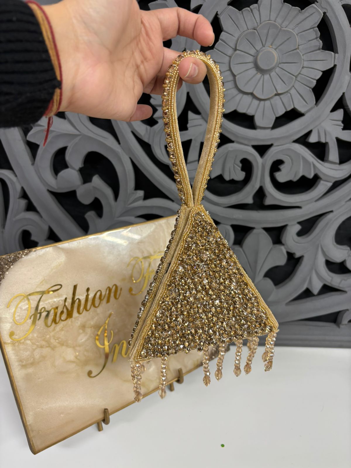 Gold beaded handbag held by a hand with a decorative background