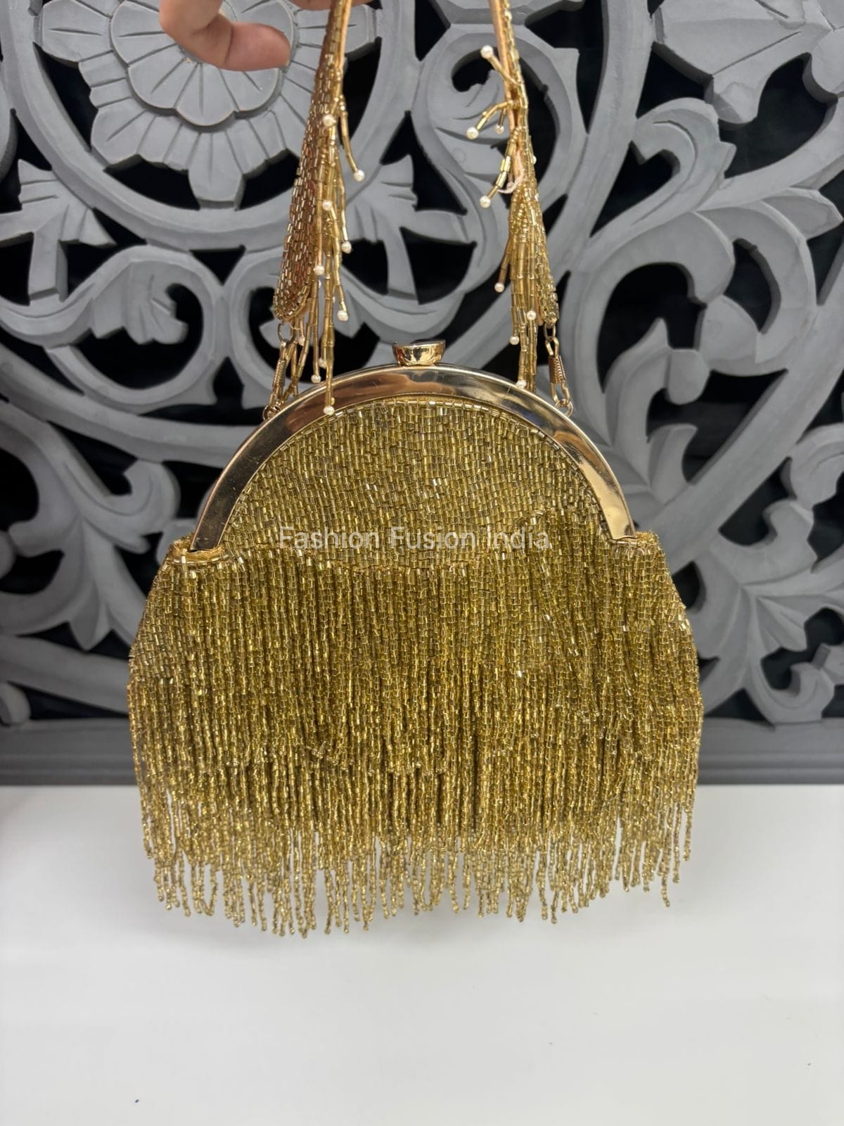 Gold beaded handbag with fringe details against a decorative black and white background.