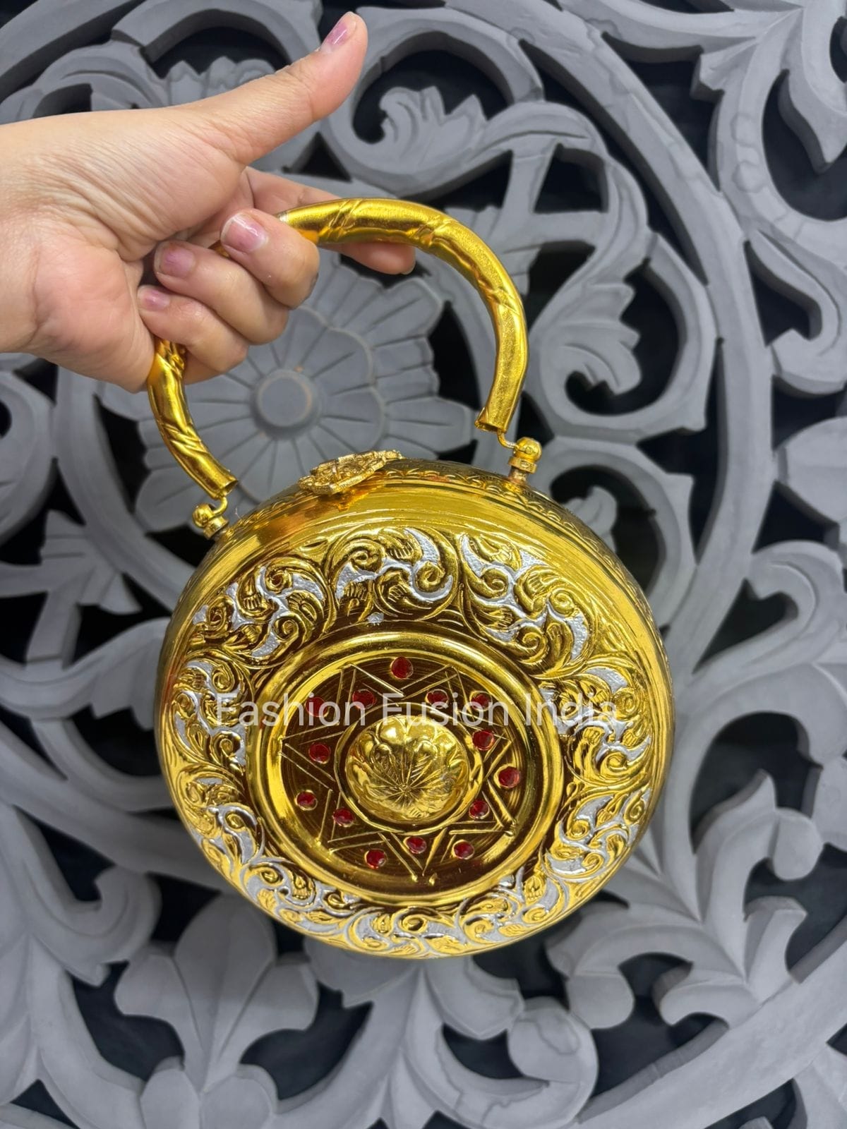 Decorative gold and silver handbag held by a hand against an ornate background