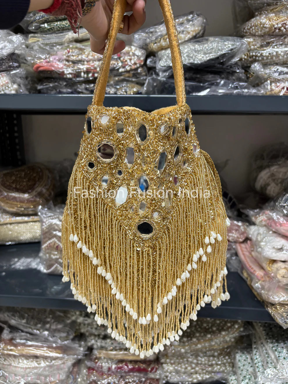 Gold beaded handbag with tassels held by a hand against a blurred background of similar bags.