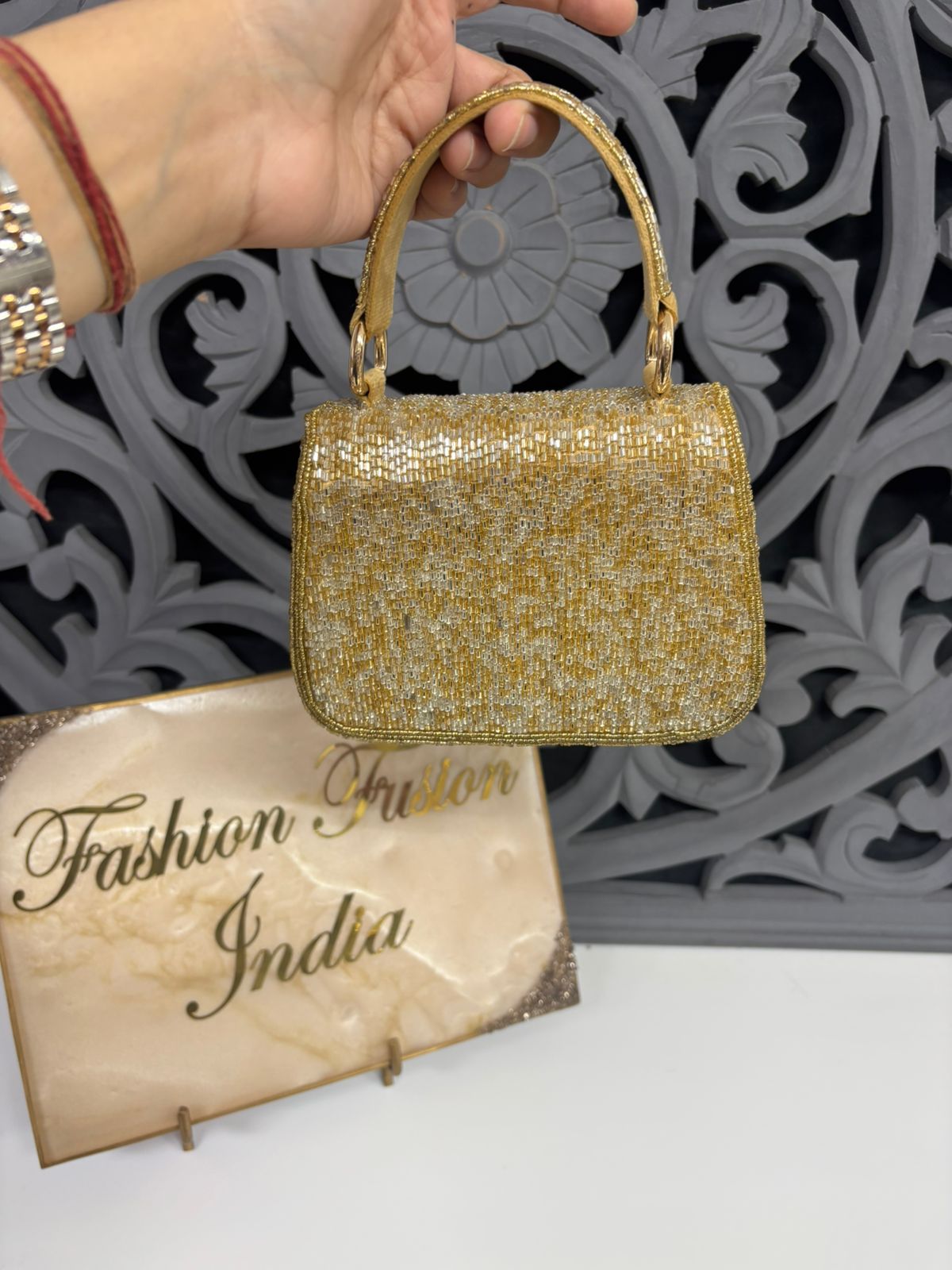 Gold glitter handbag held by a hand with a decorative background and 'Fashion Fusion India' sign.