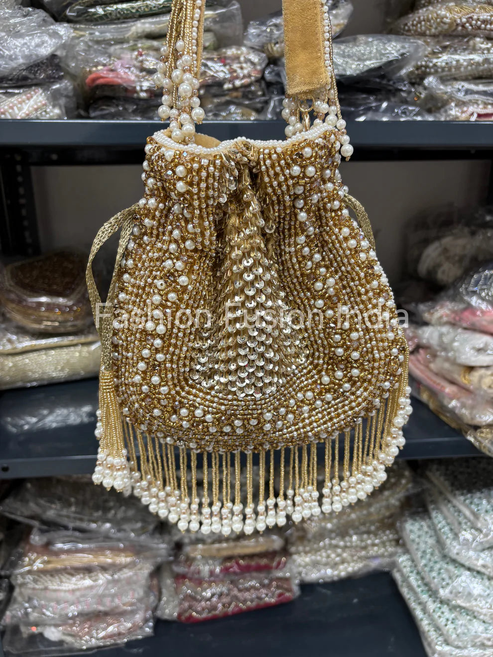 Gold beaded handbag with white pearls on a blurred background of similar bags.