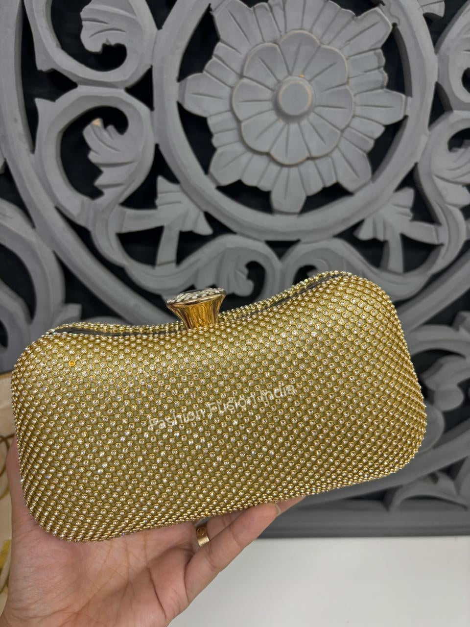 Gold clutch held by a hand with decorative background
