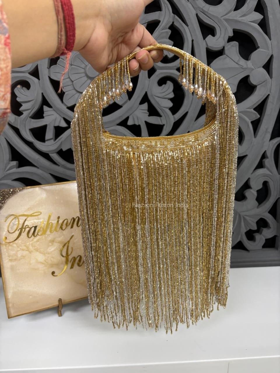 Gold fringe handbag held by a hand with a decorative background