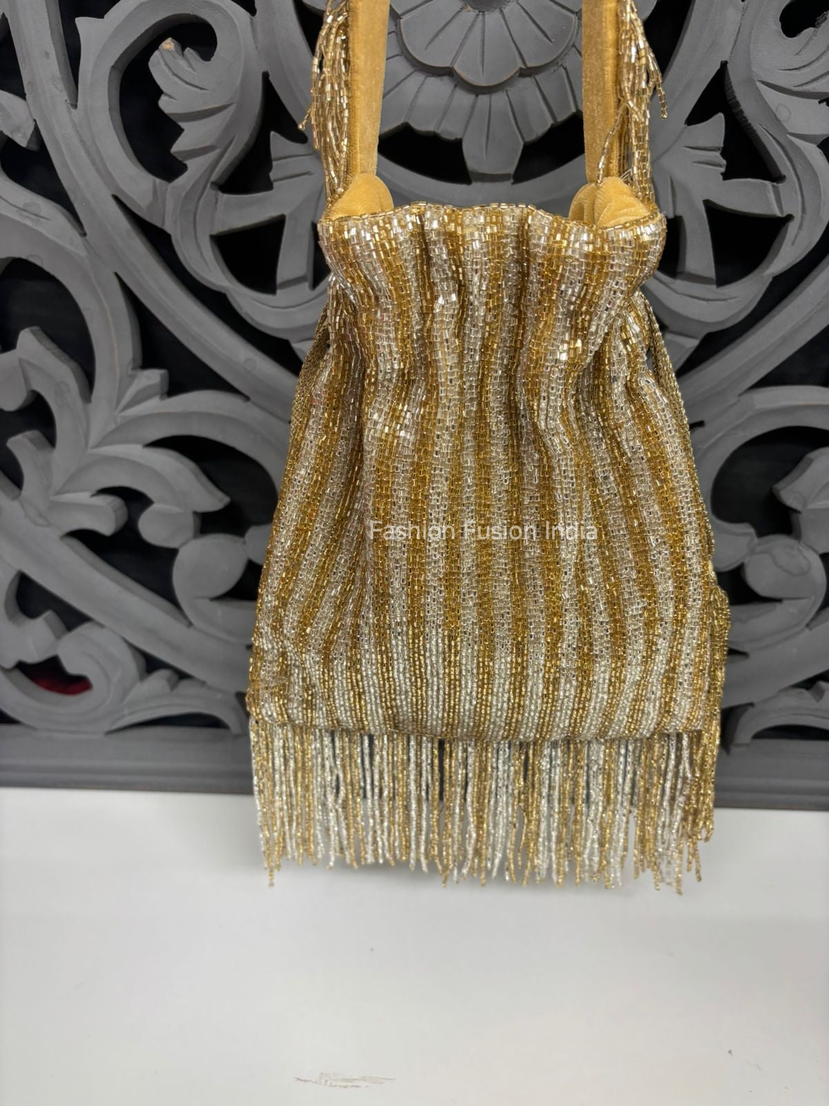Gold-silver beaded potli bag with textured vertical design, soft gathered shape aur bottom par shimmering fringe tassels