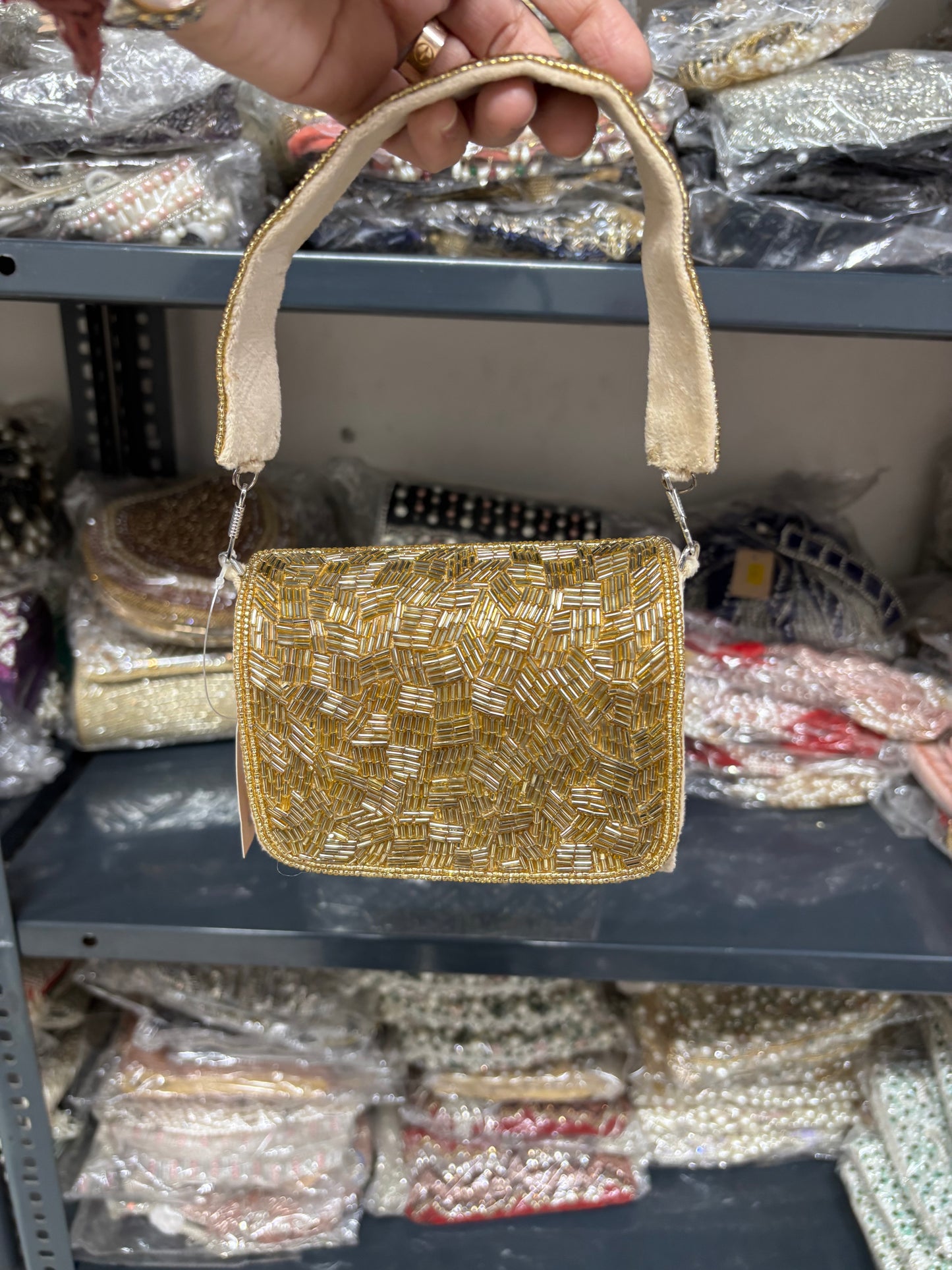 Gold beaded handbag held by a hand with a blurred store shelf in the background