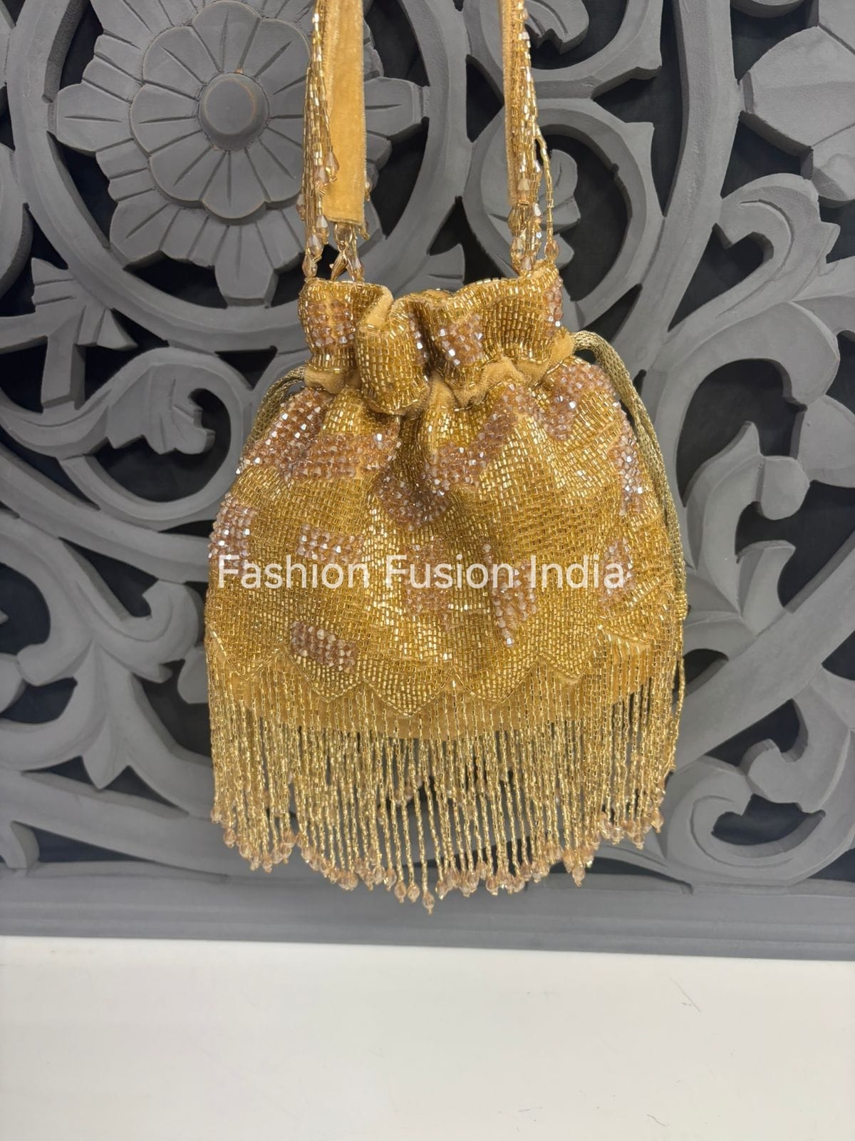 Gold beaded handbag with fringe against a decorative gray background, branded 'Fashion Fusion India'.