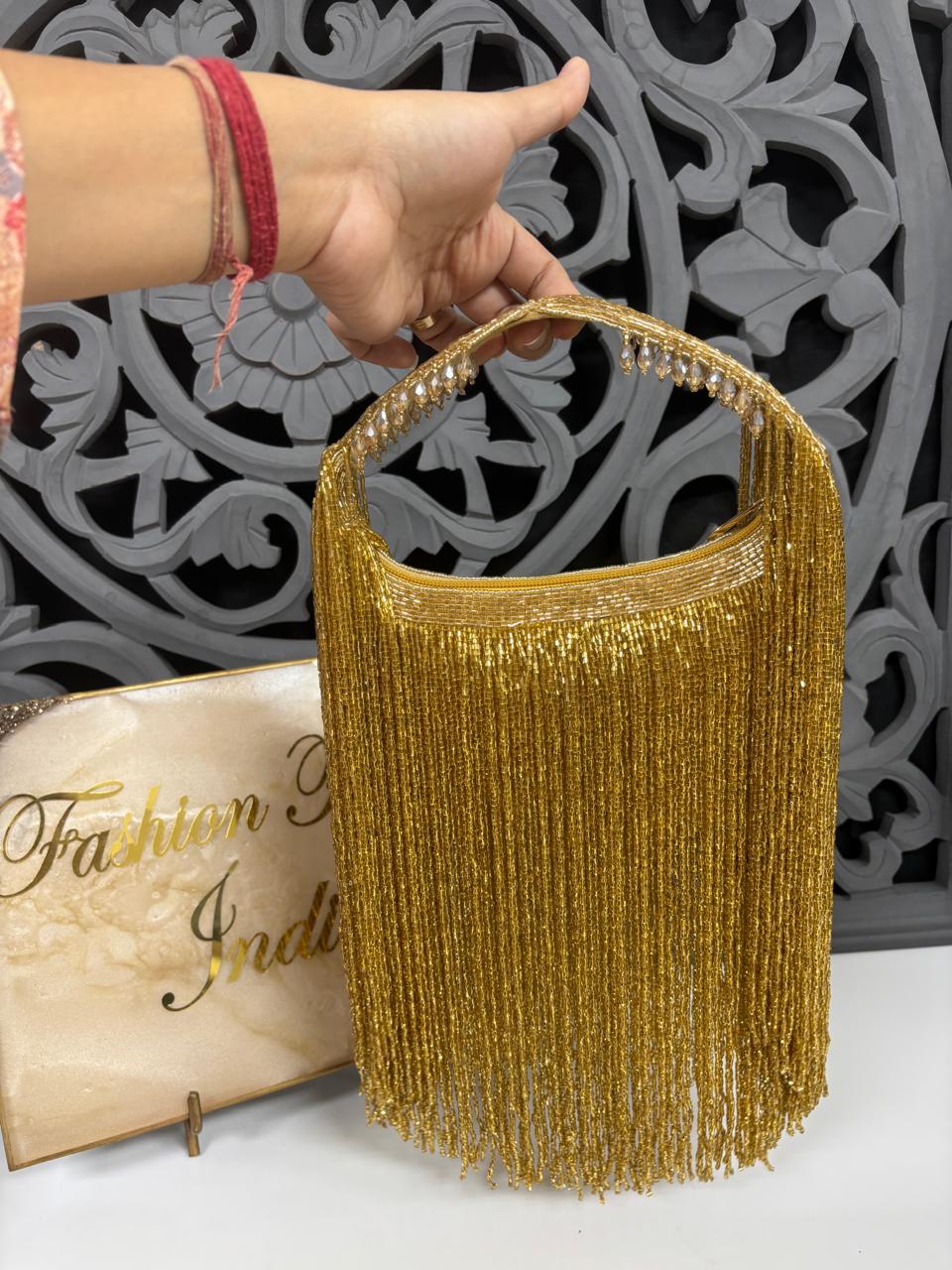 Gold fringe handbag held by a hand with a decorative background