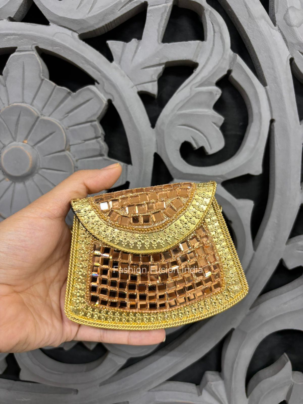 Gold and brown patterned pouch held by a hand against an ornate gray background