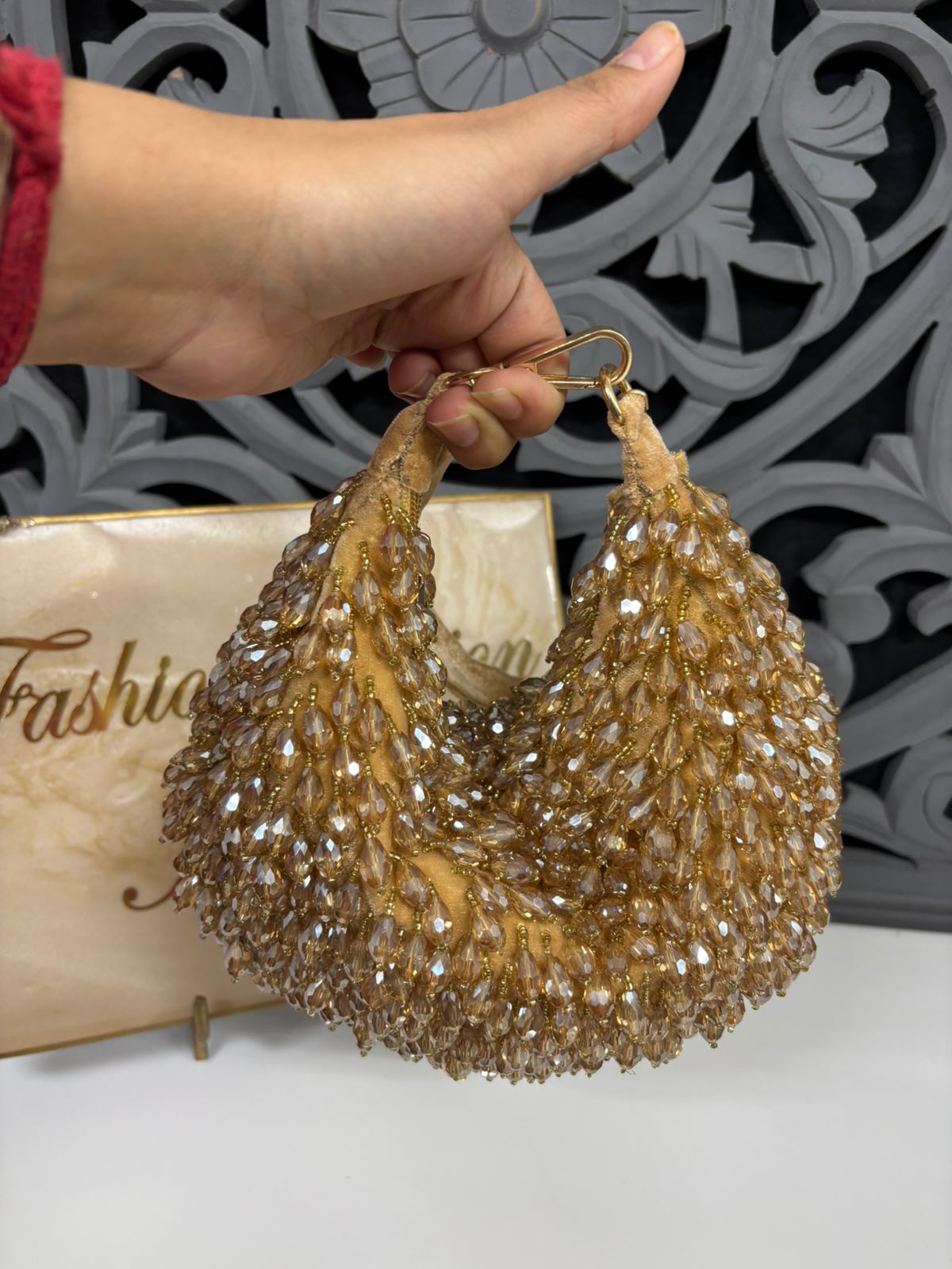 Gold beaded earrings held by a hand with a decorative background