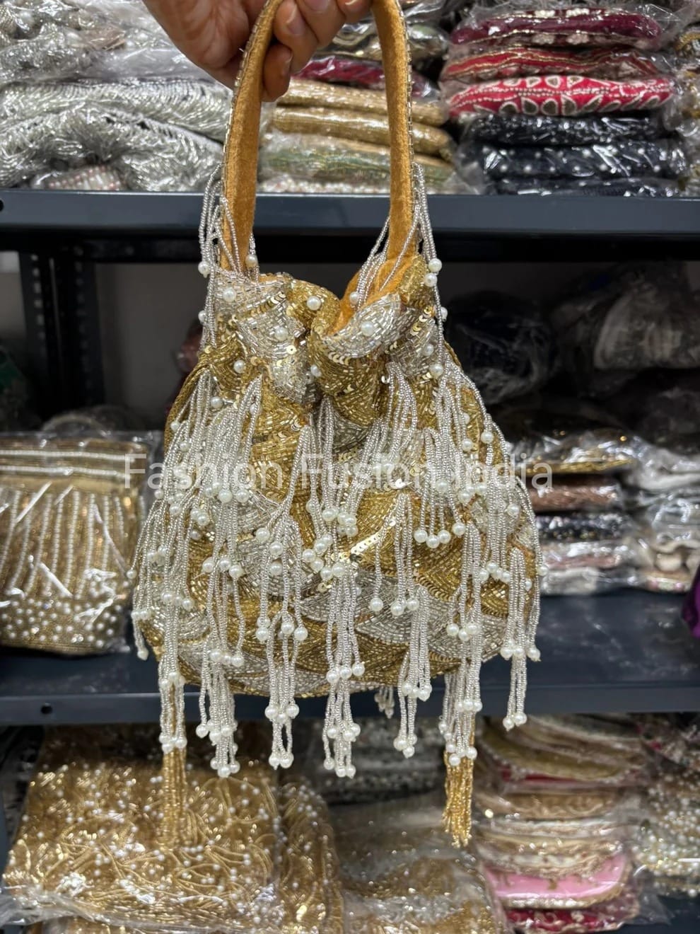 Gold and silver beaded handbag held by a hand with a blurred background of similar bags.