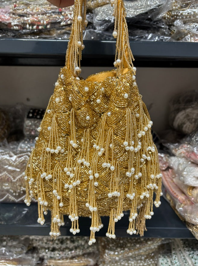 Gold beaded handbag with pearls on a reflective surface