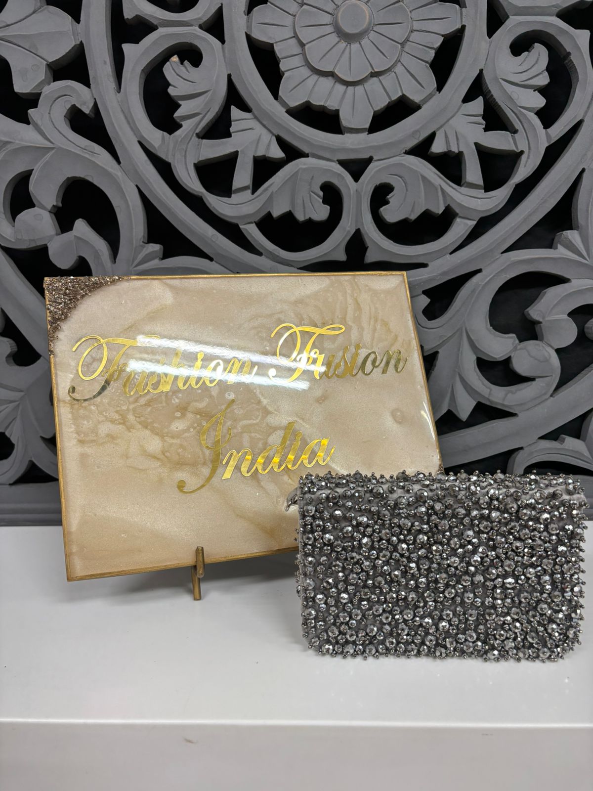 Silver clutch bag in front of a decorative box with 'Western Fashion India' text.