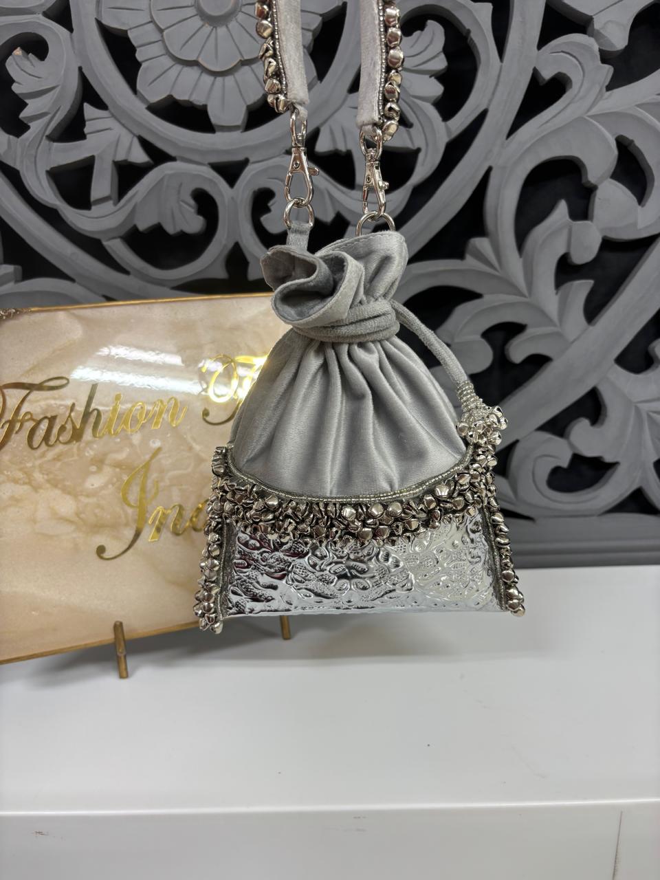 Gray handbag with decorative elements on a stand against a decorative wall.