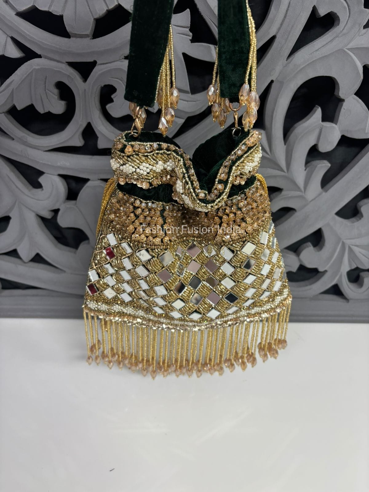 Decorative handbag with gold fringe and intricate design against a decorative wall.