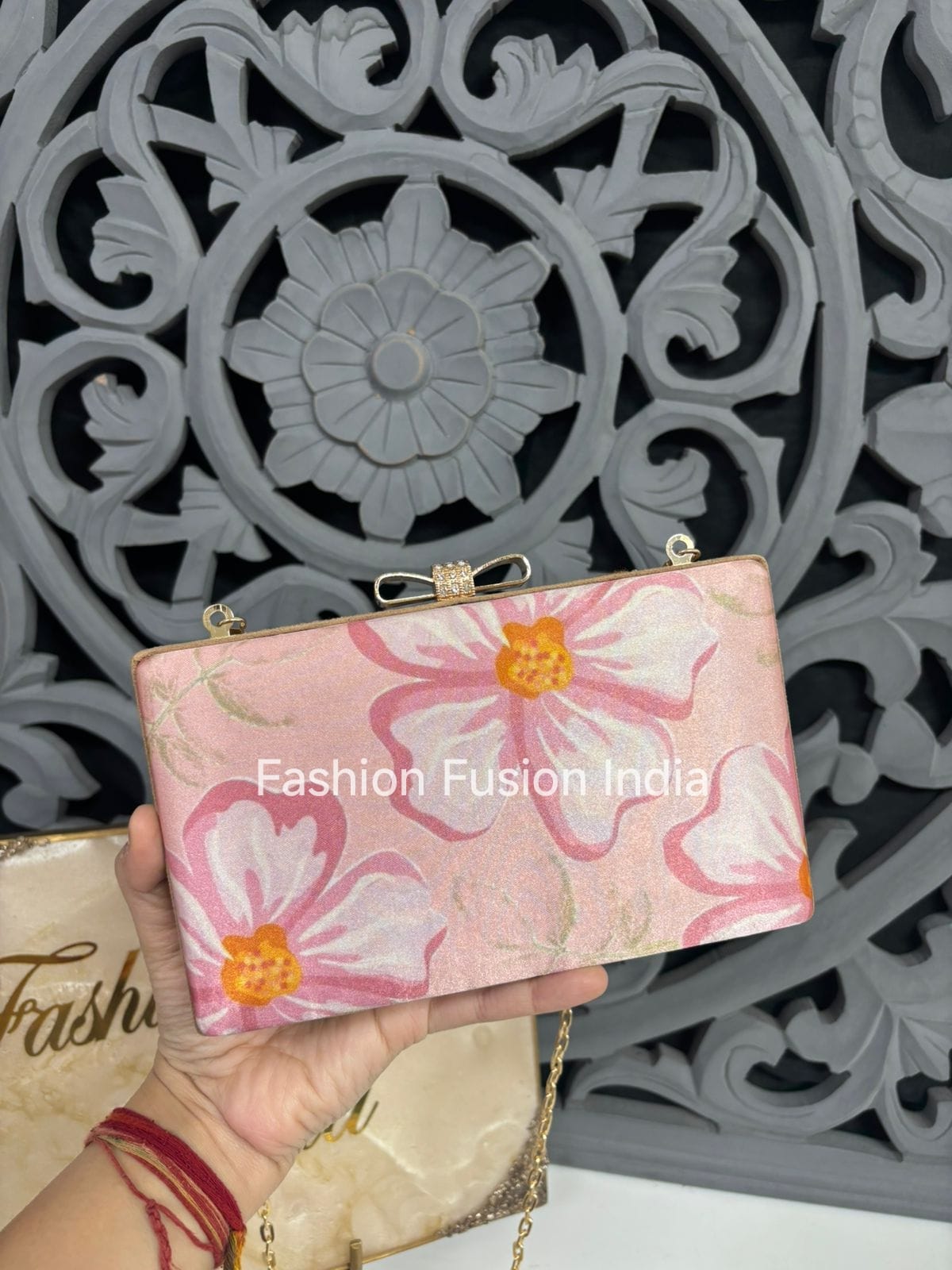 Handheld pink floral clutch with gold accents against a decorative gray background